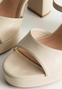 Beige plattform sandaler med en slät läderöverdela, bred rem över tårna och blockklackdesign. Mjuk texturerad insida.