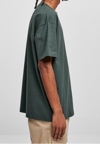 Tmavě zelené tričko s krátkým rukávem z bavlny, které má volný střih, kulatý výstřih a minimální švy.