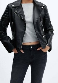 Czarna skórzana kurtka motocyklowa z srebrnymi suwakami, żebrowanymi detalami na ramionach i krótkim krojem, zestawiona z szarą bluzką i czarnymi dżinsami.