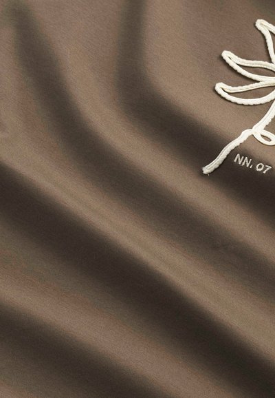 Bruine stof met een gladde textuur heeft een witte geborduurde bloemmotief en de tekst "NN. 07", wat zorgt voor een subtiel contrast.