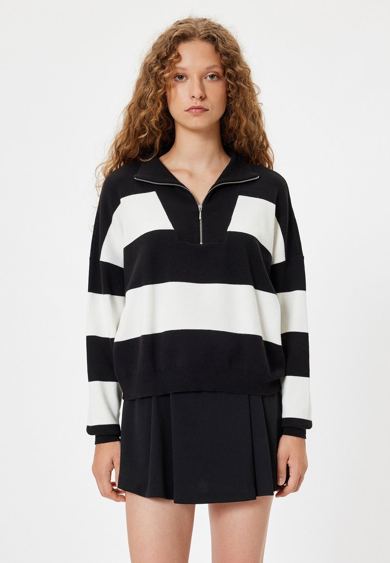 Schwarz-weiß gestreifter Pullover mit einem Reißverschlusskragen, oversized Schnitt und gerippten Bündchen, kombiniert mit einem schwarzen, plissierten Rock.