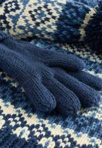 Mörkblå stickade handskar med strukturerad väv, med femfingersdesign, placerade på en mönstrad stickad bakgrund i blå och krämfärger.