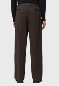 Bruine wijde broek met twee achterzakken met ritsen, knoopsluitingen en een effen textuur. Ontworpen voor comfort en veelzijdigheid.