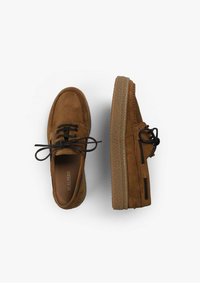 Brune ruskindssko med snørebånd, der har en struktureret sål og sidebånd. Rund tå og flad profil, velegnede til afslappet brug.