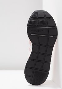 Musta kumipohja, jossa on tekstuuri ja segmentoitu kuvio, sekä Adidas-logo kohokuvioituna lähellä kantapäätä.