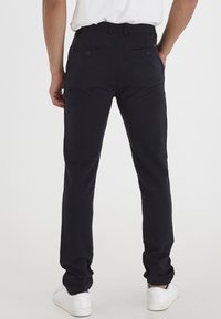 Pantaloni scuri in navy realizzati in tessuto morbido, con taglio dritto, due tasche posteriori e vita con passanti per la cintura. Indossati con scarpe da ginnastica bianche.