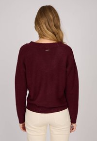Pull bordeaux avec une coupe ample, un ourlet côtelé et un large encolure, fabriqué à partir d'un tissu tricoté doux avec un petit logo dans le dos.