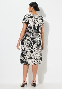 Czarna sukienka z kremowym nadrukiem roślinnym, krótki rękaw, do kolan, dopasowany krój, w połączeniu z czarnymi szpilkami. Gładka tekstura, minimalne detale.