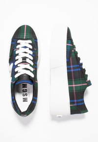 Tenisky se vzorem káro v zelené, černé, modré a růžové barvě, s bílými tkaničkami a silnou bílou podrážkou. Uvnitř je viditelná značka.