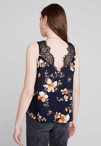 Blommig linne med mörk marinblå bas, orange och vita blommor samt en spetsbak med V-formad utskärning. Slät tyg och åtsittande design.