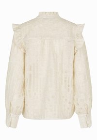 Long-sleeve, cream blouse made of textured fabric. Features ruffled shoulder accents and a high neckline with subtle patterned detailing.