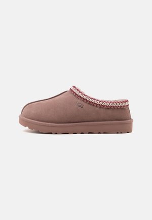 Chaussons UGG marron à enfiler avec bordure tressée et doublure douce, semelle plate et logo UGG sur le côté.