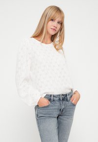 Witte blouse met lange mouwen, voorzien van een bloemmotief en pofmouwen, gecombineerd met lichtblauwe high-waisted jeans. Glad materiaal.