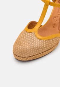Chaussure plate pour femme beige à motifs avec bride en T en cuir jaune et bout arrondi, présentée sur fond blanc uni.