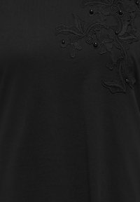 Sort stof med indviklet blomsterblondeapplikation og små sorte perler samlet i øverste højre sektion.