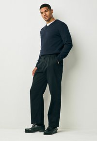 Pulover navy cu decolteu în V, pantaloni negri plisati, și pantofi negri cu șireturi. Texturi netede și o croială relaxată. Scheme de culori simple.