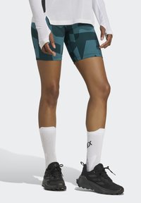 Teal- och svarta mönstrade shorts med en tight passform, parat med vita ankelsockor och svarta träningsskor. Fokusera på detaljer i designen av aktivkläder.