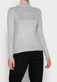 Grå polo som är gjord av mjukt, stickat tyg, med långa ärmar och ribbat krage, ihopparat med mörka byxor.