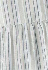 Lekka tkanina z pionowymi szarymi i białymi paskami, z marszczonym wykończeniem na dole, które dodaje wymiaru i wizualnego zainteresowania.