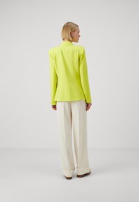 Blazer neon galben cu umeri structurați, asortat cu pantaloni evazați crem. Țesătură netedă cu o croială adaptată, design minimalist.
