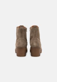 Par de botas de ante marrón hasta el tobillo con tacones de bloque vistas desde atrás sobre un fondo blanco liso.