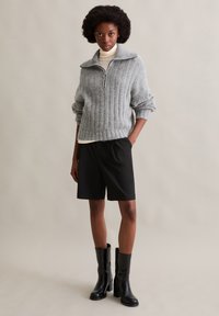 Szary sweter z prążkowanej dzianiny z kołnierzem na pół-zamek, zestawiony z czarnymi szortami i czarnymi kozakami do kolan. Gładka tekstura, luźny krój.