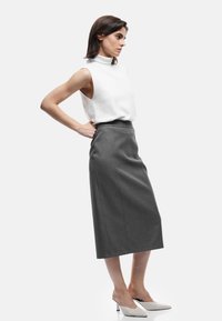 Top sin mangas de color blanco con cuello alto, combinado con una falda lápiz gris a la altura de la rodilla y mules trenzados blancos de tacón. Tela suave y corte ajustado.