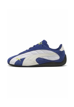 Niedrig geschnittener blauer und weißer Puma-Sneaker mit Obermaterial aus wildleder und Mesh, gelbem Puma-Logo und schwarzer Sohle, seitlich auf weißem Hintergrund gezeigt.