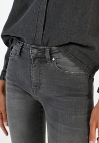 High-waisted, dark grey denim jeans with a slim fit, featuring a front button closure, five pockets, and subtle whiskering details.