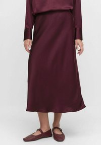 Burgunderfärgad satin midi-kjol med en slät textur, flödande design och subtil glans. Kombinationen med vinröda vävda flats med spänne.