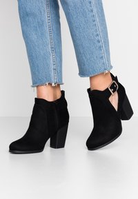 Zwarte suède enkellaarzen met een chunky hak, zijrits en cut-out ontwerp. Gecombineerd met lichtblauwe denim jeans met rafelige zoom.