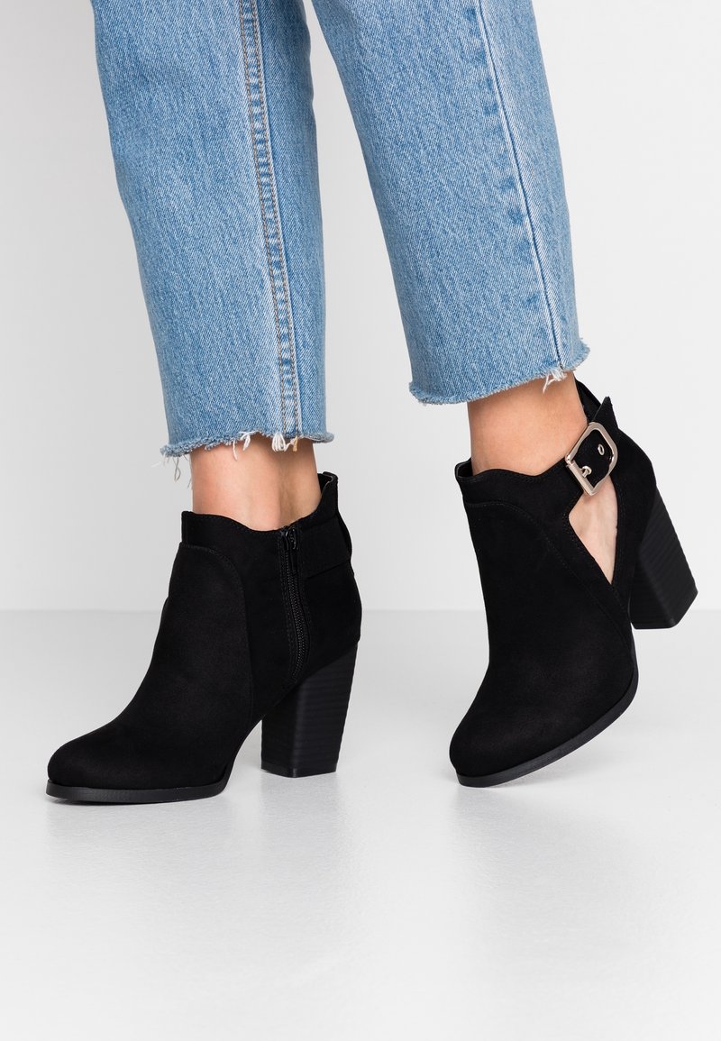 Zwarte suède enkellaarzen met een chunky hak, zijrits en cut-out ontwerp. Gecombineerd met lichtblauwe denim jeans met rafelige zoom.