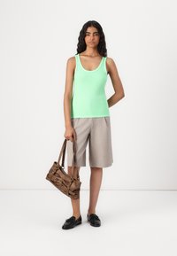 Light green ribbed tank top with white trim, gray pleated shorts, brown shoulder bag, and black loafers. Model stands posed against white backdrop.