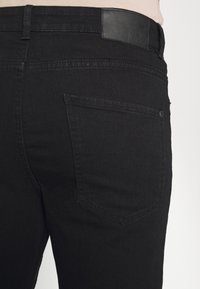 Jeans in denim nero con una texture liscia, tasche posteriori e un'etichetta logo discreta in vita. Design elegante e minimalista.