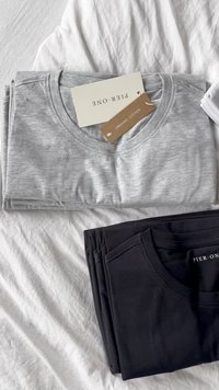 Gray and black organic cotton T-shirts, neatly folded, showing round necklines and brand tags. Textured fabric, minimalistic design.
