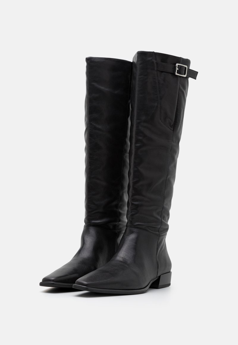 Bottes noires jusqu'aux genoux en cuir, avec un bout pointu, un talon carré plat et une sangle réglable avec une boucle sur le côté supérieur.