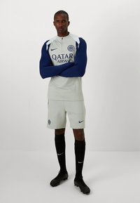 Camisola desportiva cinza com mangas azuis, com o logotipo da 'Qatar Airways' e emblema da equipa. Combinada com calções cinza e meias pretas.