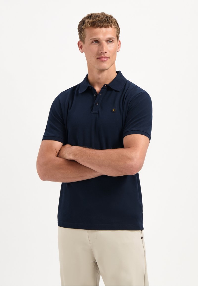 Marineblauwe polo gemaakt van zachte stof, met een klassieke kraag, drie-knoopsluiting en een klein logo op de borst.