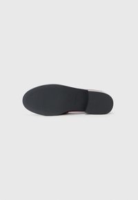 Black rubber shoe sole with horizontal ridges, featuring a slight heel and red accent around the base. Smooth texture overall.