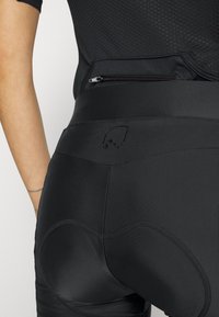 Czarne spodenki rowerowe z gładkiego, elastycznego materiału. Cechy obejmują wyściełane akcenty oraz małe wytłoczone logo na pasie.