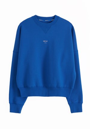 Sininen pyöreäkauluksinen collegepaita, jossa on pitkät hihat ja pieni valkoinen "aimn"-logo rinnan keskellä. Resorit hihansuissa ja helmassa.