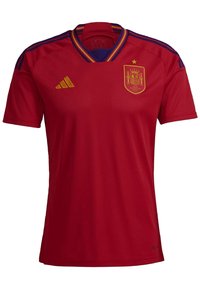 Červený fotbalový dres s výstřihem do V, zlatým logem Adidas a znakem národního týmu Španělska. Modré a zlaté detaily na rukávech.