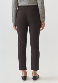 Donkerbruine broek gemaakt van rekbare stof, met een slim fit, twee achterzakken en een nette tailleband. Draagt met zwarte platte schoenen.