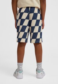 Blå och krämfärgade rutiga shorts i mjukt material, med avslappnad passform och sidofickor. Matchas med vita sneakers och grå strumpor.