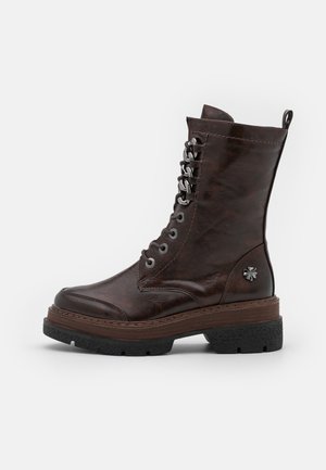 Botte de combat en cuir marron foncé à lacets avec œillets métalliques, languette au talon, logo décoratif sur le côté et semelle épaisse en caoutchouc noir.
