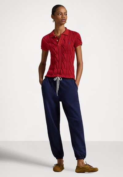 Rdeča polo majica s kitami, s kragnom, združena z mornarsko modrimi trenirkami. Bež mokasini s elastičnim pasom na hlačah.