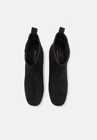 Botines de ante negro con una textura suave, puntera redondeada y una tira en la parte posterior para facilitar su uso.