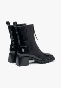 Zwarte enkellaarzen van lakleer met een puntige neus, ritssluiting en stevige geribbelde hakken. Twee aantreklusjes aan de achterkant voor gemakkelijk aan- en uittrekken.