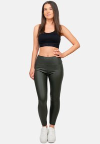 Leggings aderenti a vita alta in materiale elasticizzato di colore verde oliva, abbinati a un crop top nero e sneakers bianche. Texture morbida, design aderente.