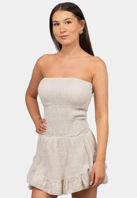 Beige strapless jurk met een gestructureerde, gerimpelde bovenkant en een uitlopende, rimpelige rok. Het materiaal lijkt lichtgewicht en ademend.